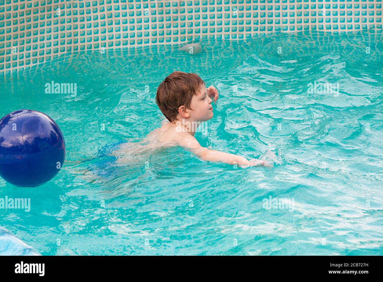 Happy kid playing in the swimming pool. Having fun with ball in water pool outside on summer day. Leisure and swimming at holidays. Happiness and joy Stock Photo