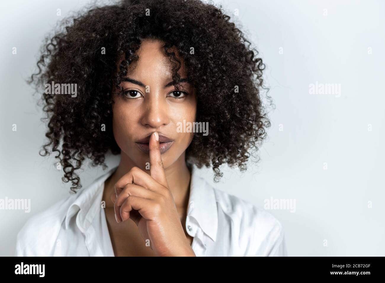 beautiful afro-american woman doing gesture of silence with finger in lips with white background Stock Photo
