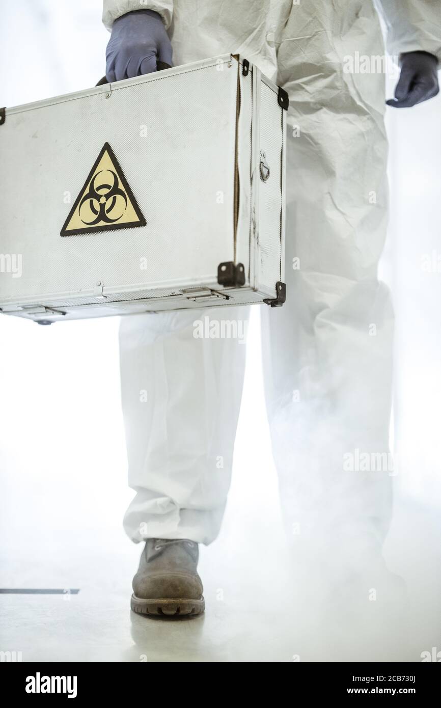 Corona virus concept. Male scientist doctor in latex gloves and protective suit holds analysis case with biohazard sign during COVID pandemic outbreak Stock Photo