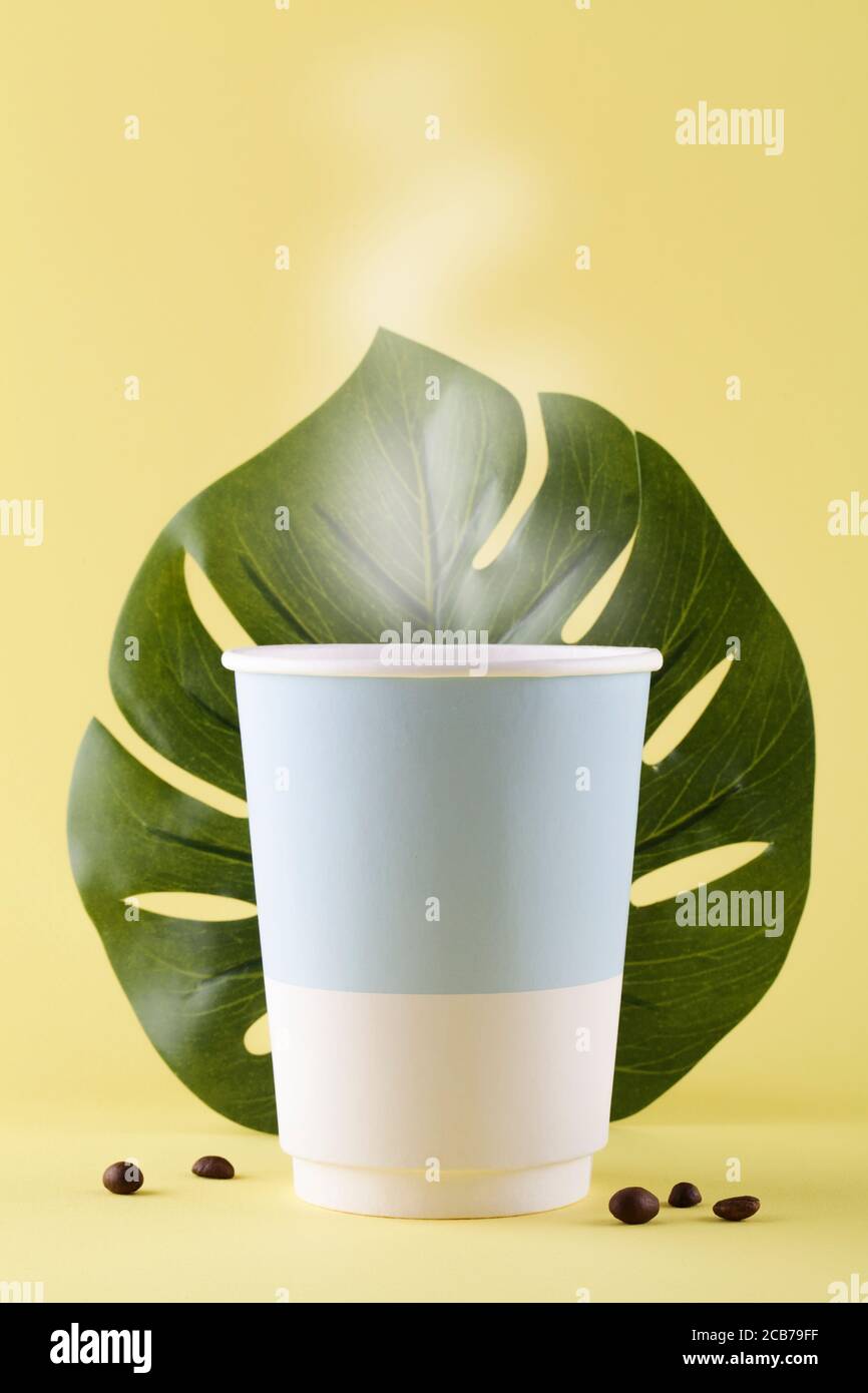 take away paper cup for coffee with steam, coffee beans and monstera ...
