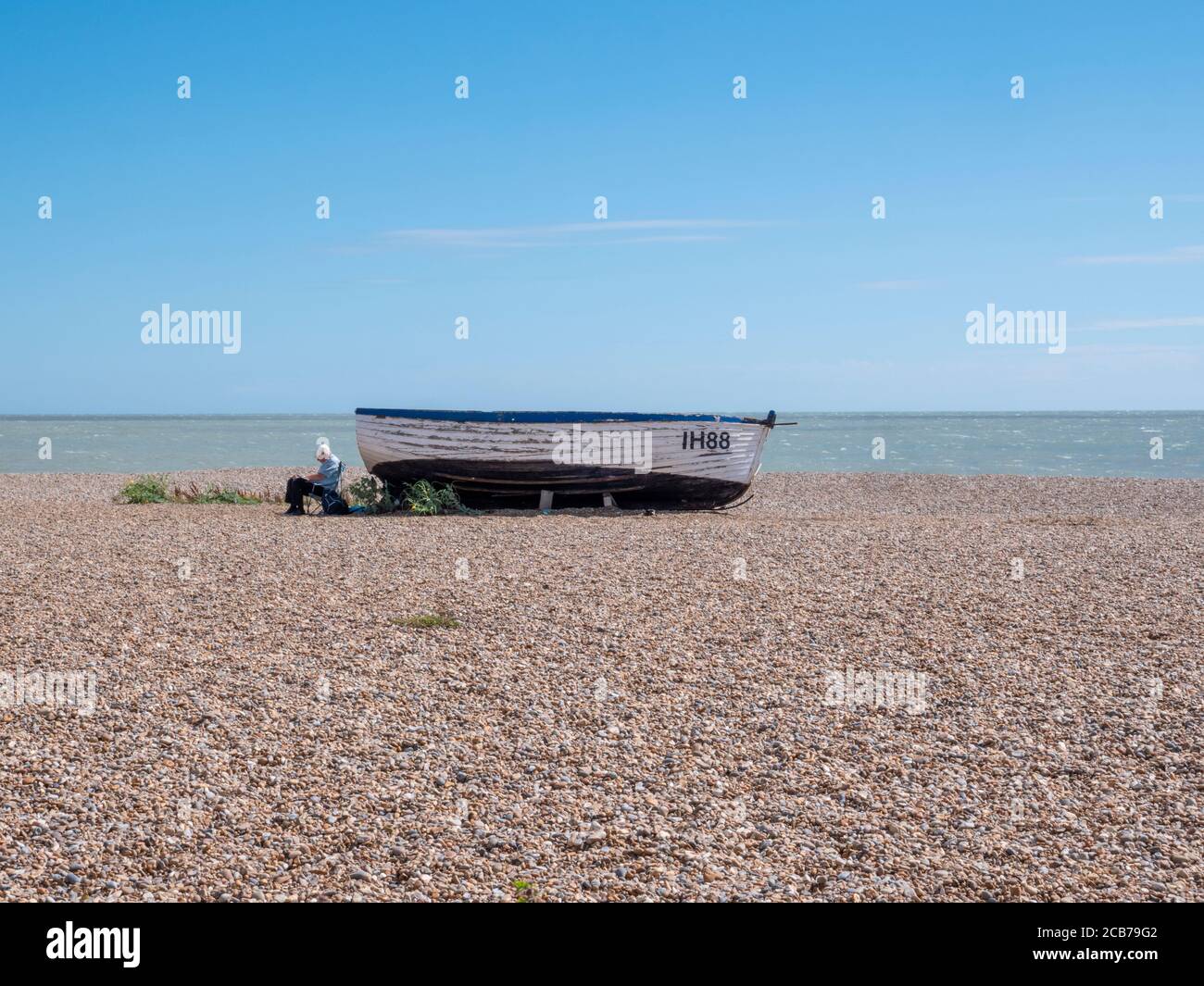 A man sitting next to an old fishing boat on the shingle beach at ...