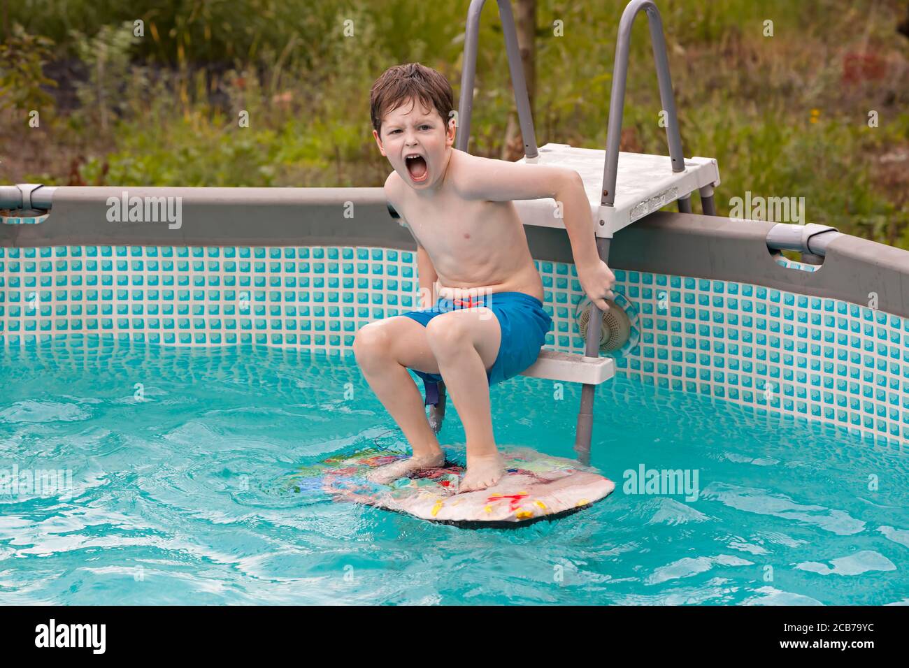 Happy kid excited about jumping in the swimming pool. Having fun in water pool outside on summer day. Leisure and swimming at holidays. Happiness and j Stock Photo