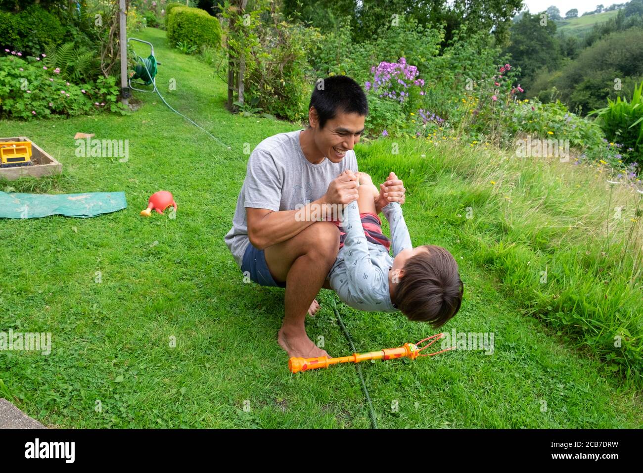Father crouching on lawn grass in country garden playing holding balancing his 3 year old son child boy in summer garden Wales UK KATHY DEWITT Stock Photo