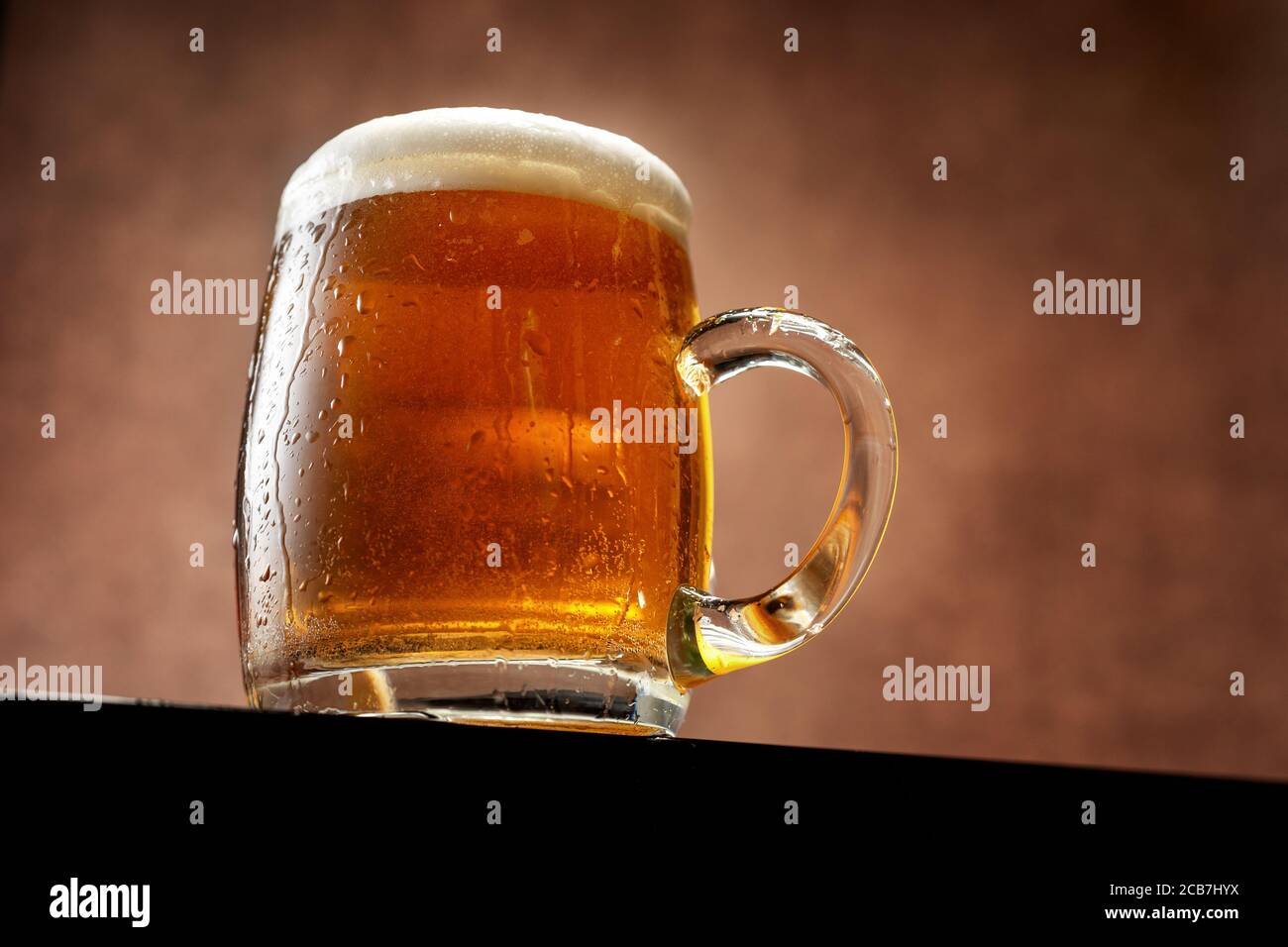 Mug of beer with foam standing against brown background Stock Photo