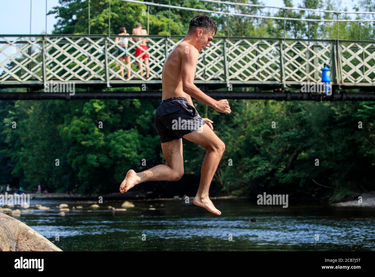 A person jumps from a rock into the River Wharfe near Ilkley in Yorkshire, as people continue to enjoy the hot weather. Stock Photo
