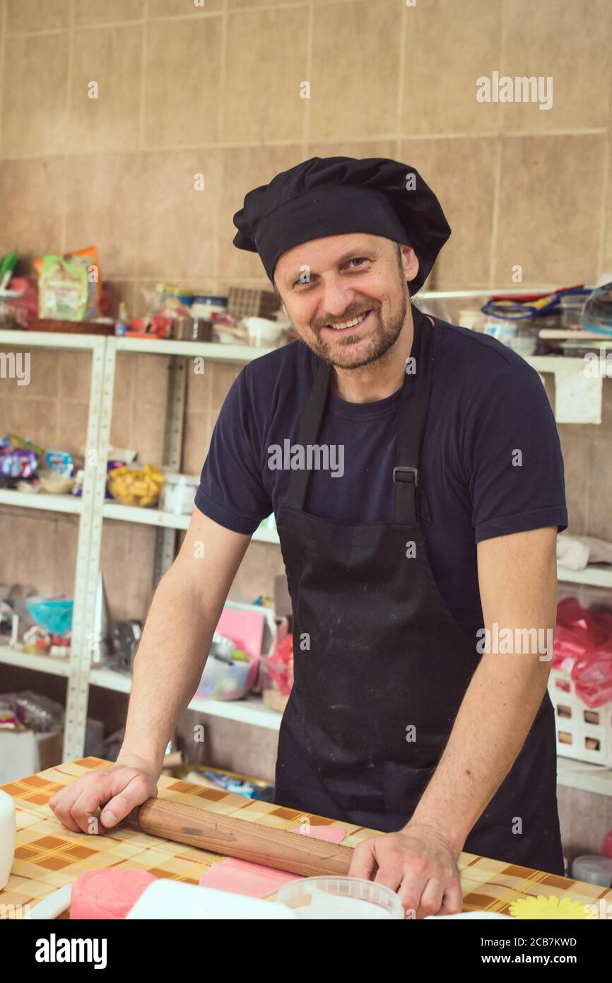 Male pastry chef using rolling pin on piece of dough. Making cake decoration Stock Photo