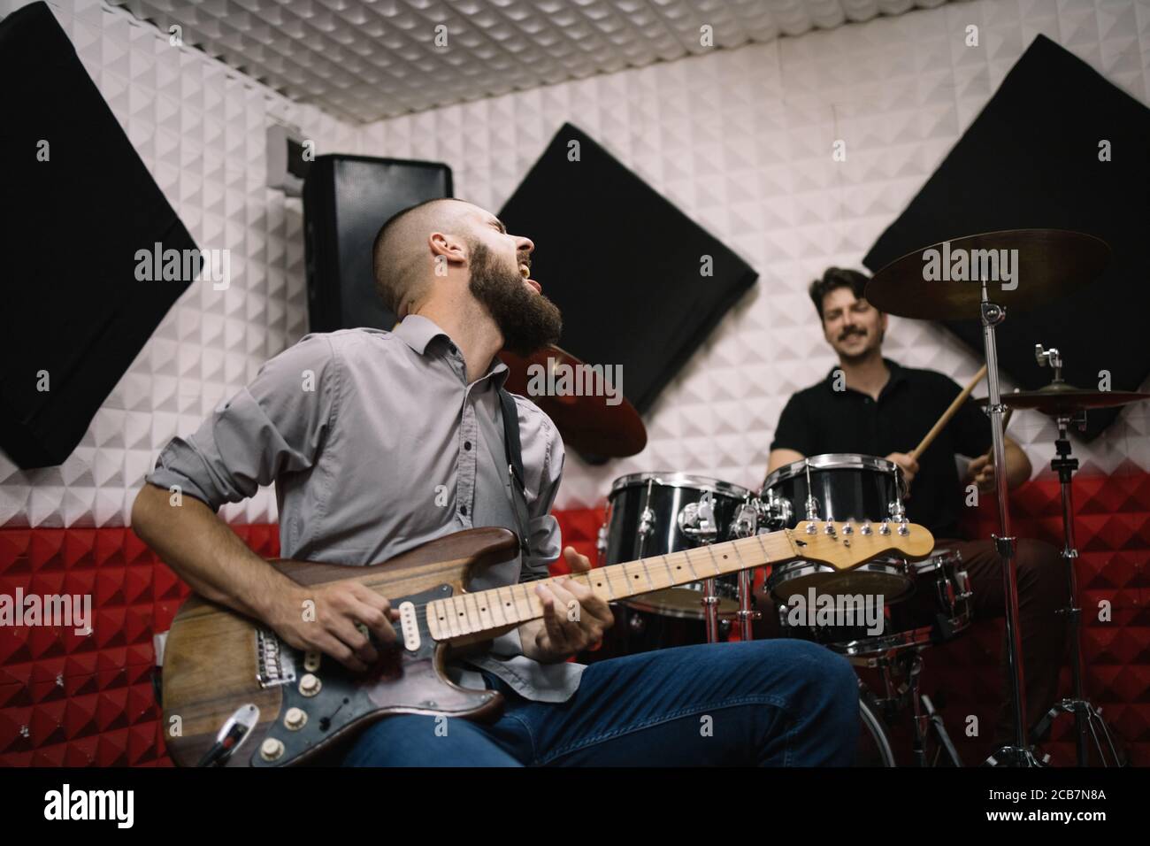 Rock band recording in soundproof music studio. Guitar player and drummer playing music