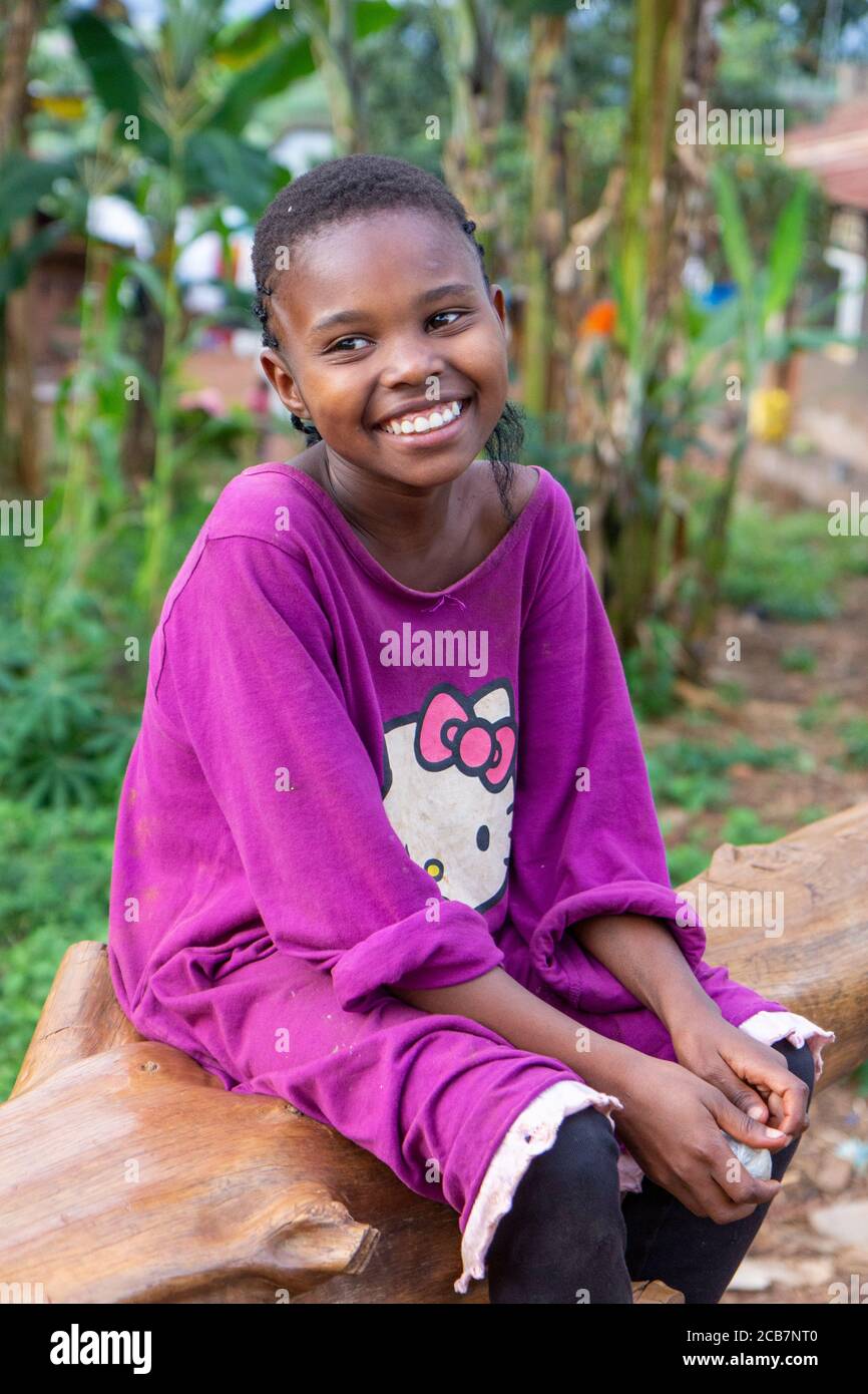 A smiling Ugandan girl sitting on a fallen tree trunk. Shot in Uganda in 2017. Stock Photo