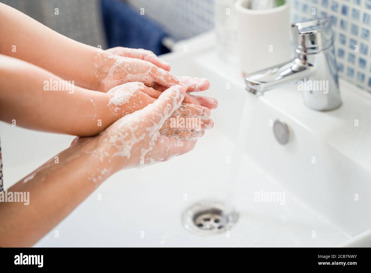 Mother helping girl child washing hands together in bathroom sink with lots of soap under running water tap Stock Photo