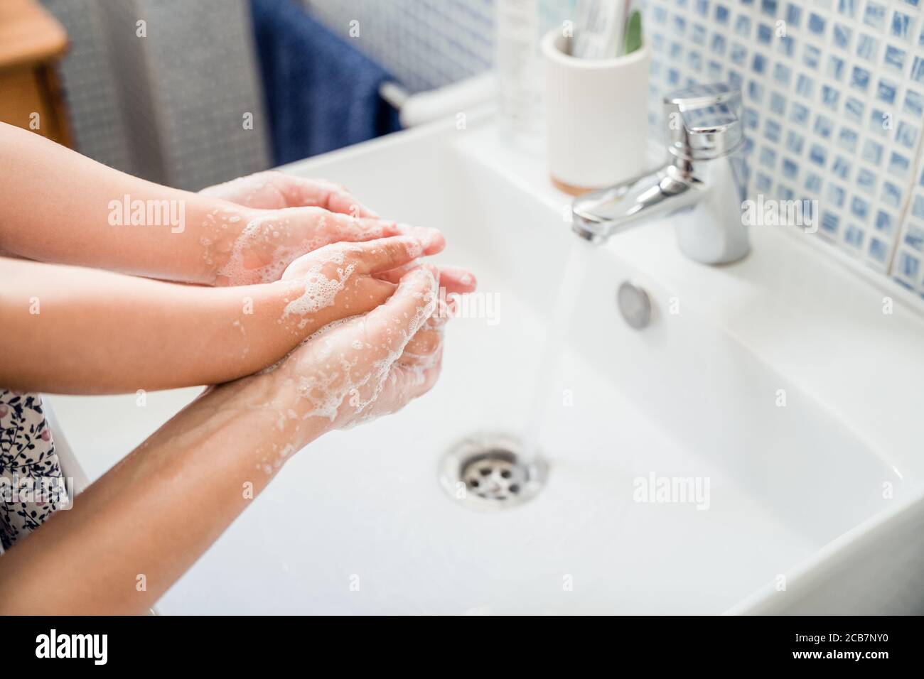 Mother and girl child washing hands together in bathroom sink with lots of soap under running water tap. Holding hands Stock Photo