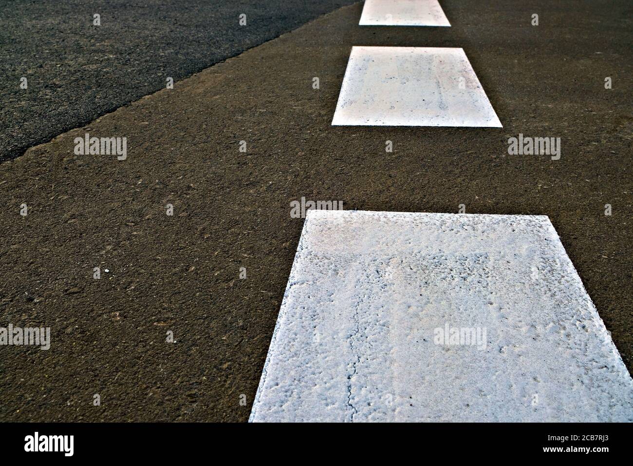 Broad dashed white line in perspective painted with reflective paint on black asphalt tarmac road. Stock Photo