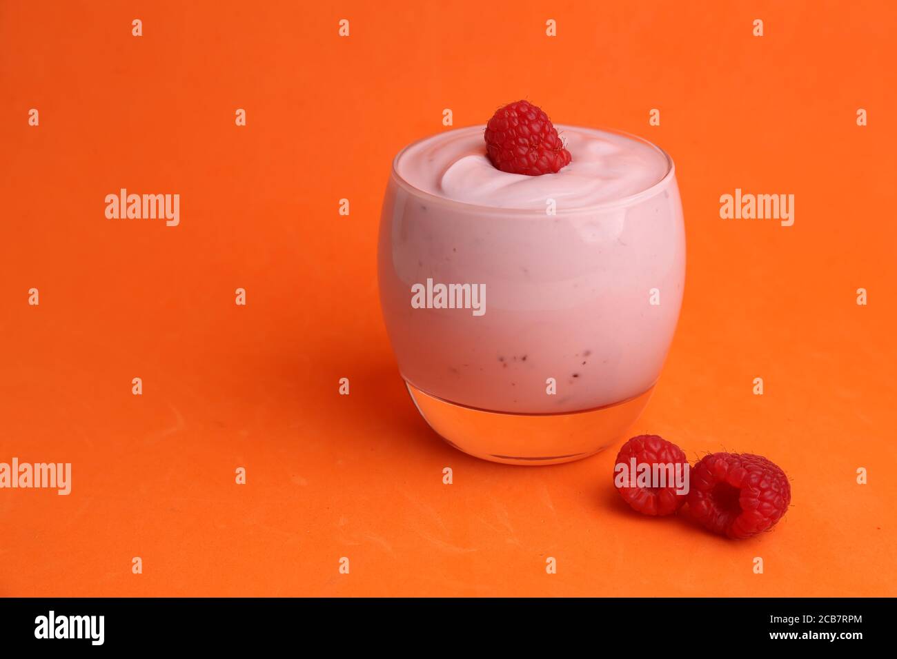 Closeup of a glass of sweet yogurt with a fresh raspberry on top on an