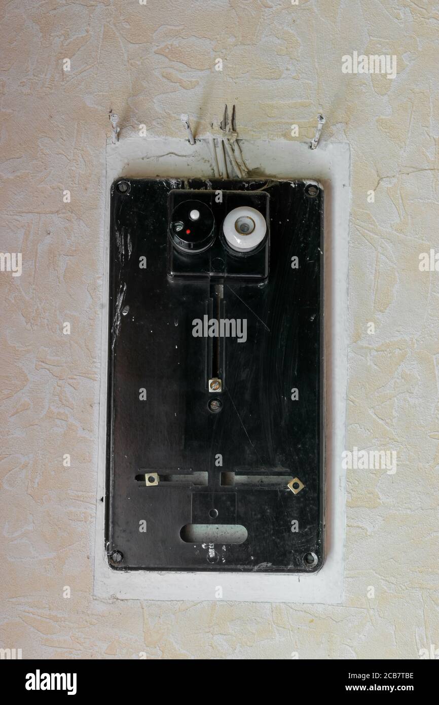 Very old black electrical fuses box hanging on white rural wall with copy space Stock Photo