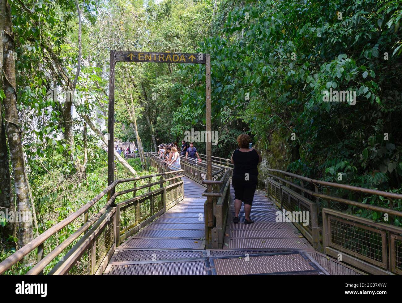 Walkway in the upper circuit of Iguazu National Park. Tourists in pathway through the forest. Entrance overhead sign. Stock Photo