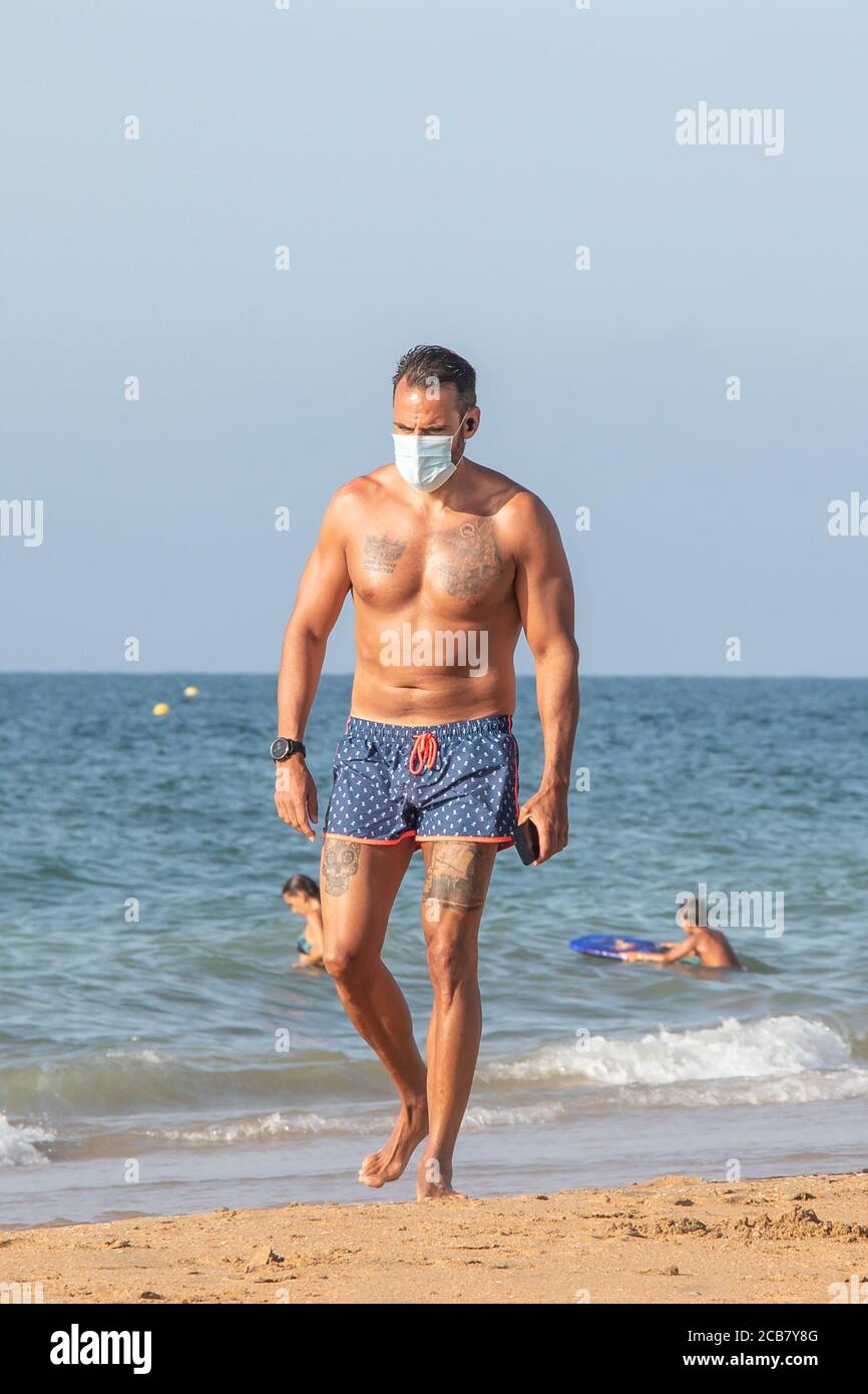 Punta Umbria, Huelva, Spain - August 7, 2020: Woman walking by the beach wearing protective or medical face masks. New normal in Spain with social dis Stock Photo