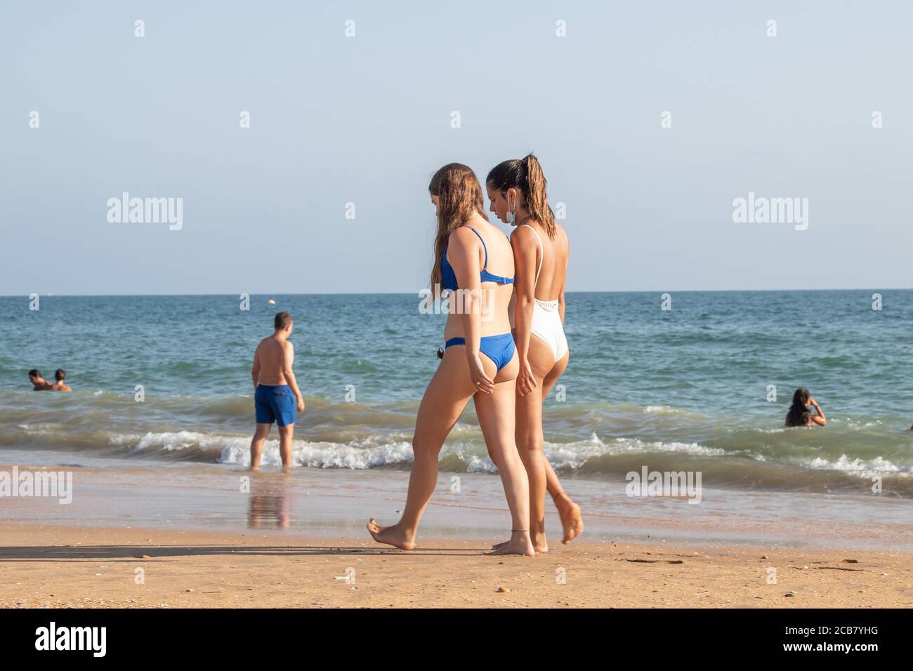 Punta Umbria, Huelva, Spain - August 7, 2020: Couple walking by the beach wearing protective or medical face masks. New normal in Spain with social di Stock Photo