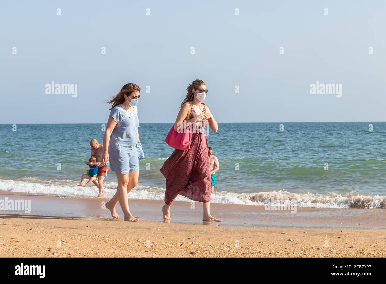 Punta Umbria, Huelva, Spain - August 7, 2020: Two woman walking by the beach wearing protective or medical face masks. New normal in Spain with social Stock Photo