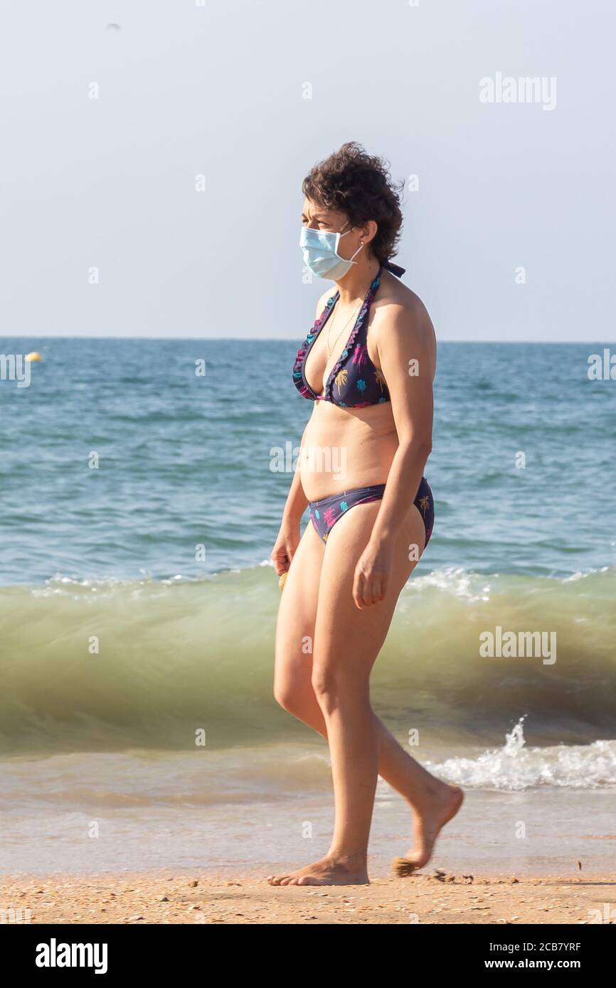 Punta Umbria, Huelva, Spain - August 7, 2020: Woman walking by the beach wearing protective or medical face masks. New normal in Spain with social dis Stock Photo