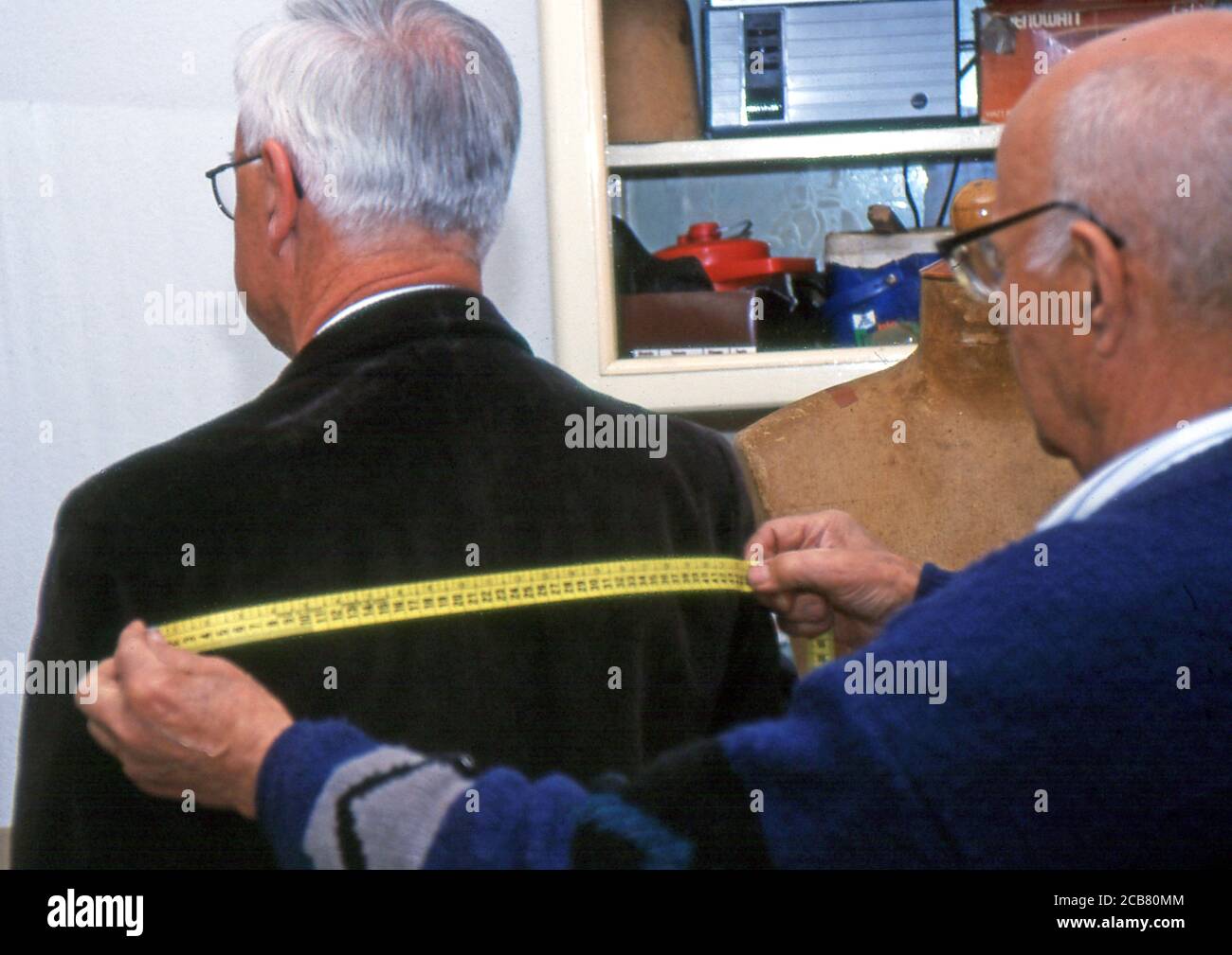 Old tailor takes measurements to a man in Sardinia (scanned from Fujichrome Provia) Stock Photo