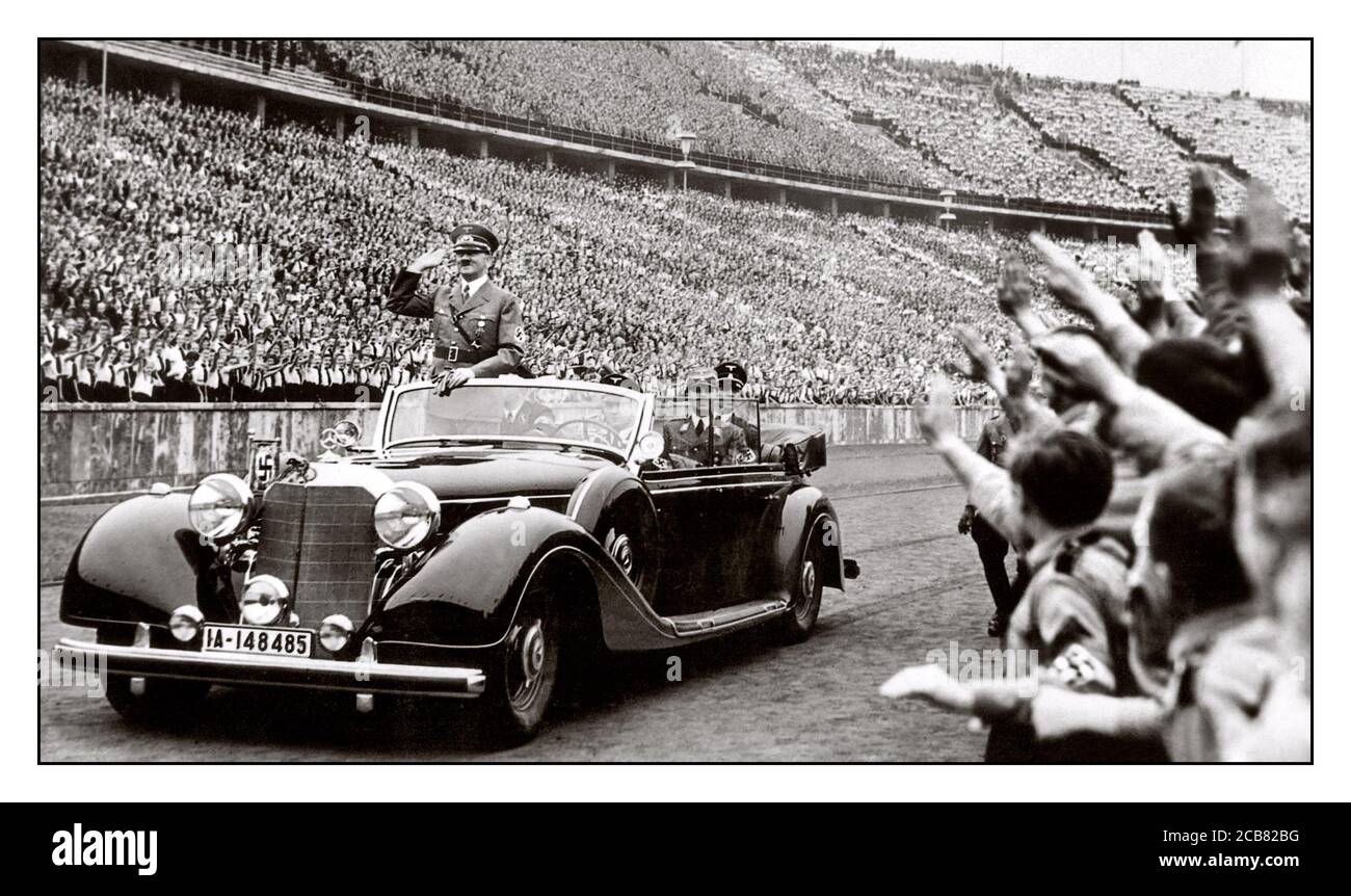NUREMBERG Adolf Hitler in uniform wearing swastika armband gives Heil Hitler salute to the military and ecstatic crowds at a huge Nazi rally in 1938 Germany. Hitler salutes attendees at a Reichsparteitag (Reich Party Day) in Nuremberg, Germany. A uniformed Martin Bormann also in attendance sitting in rear of open top Mercedes Car Stock Photo