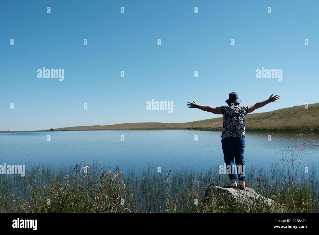 Woman standing at the edge of a lake with her arms outstretched, Auvergne, France Stock Photo