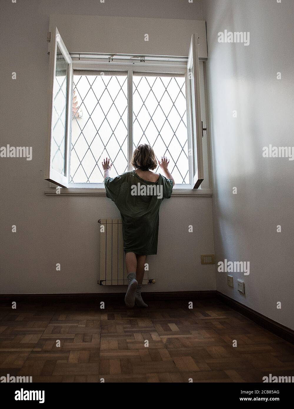 Rear view of a girl trapped in a room looking through window Stock