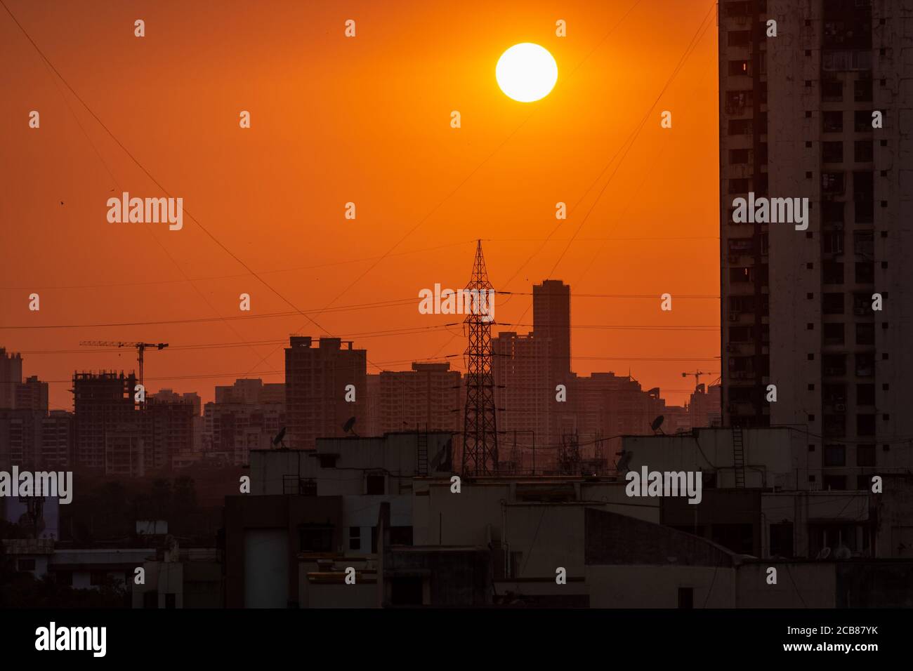 Mumbai, Maharashtra, India - March 2020: The sun setting above an electric pylon and the tall high rises of the suburb of Kandivali East in Mumbai. Stock Photo