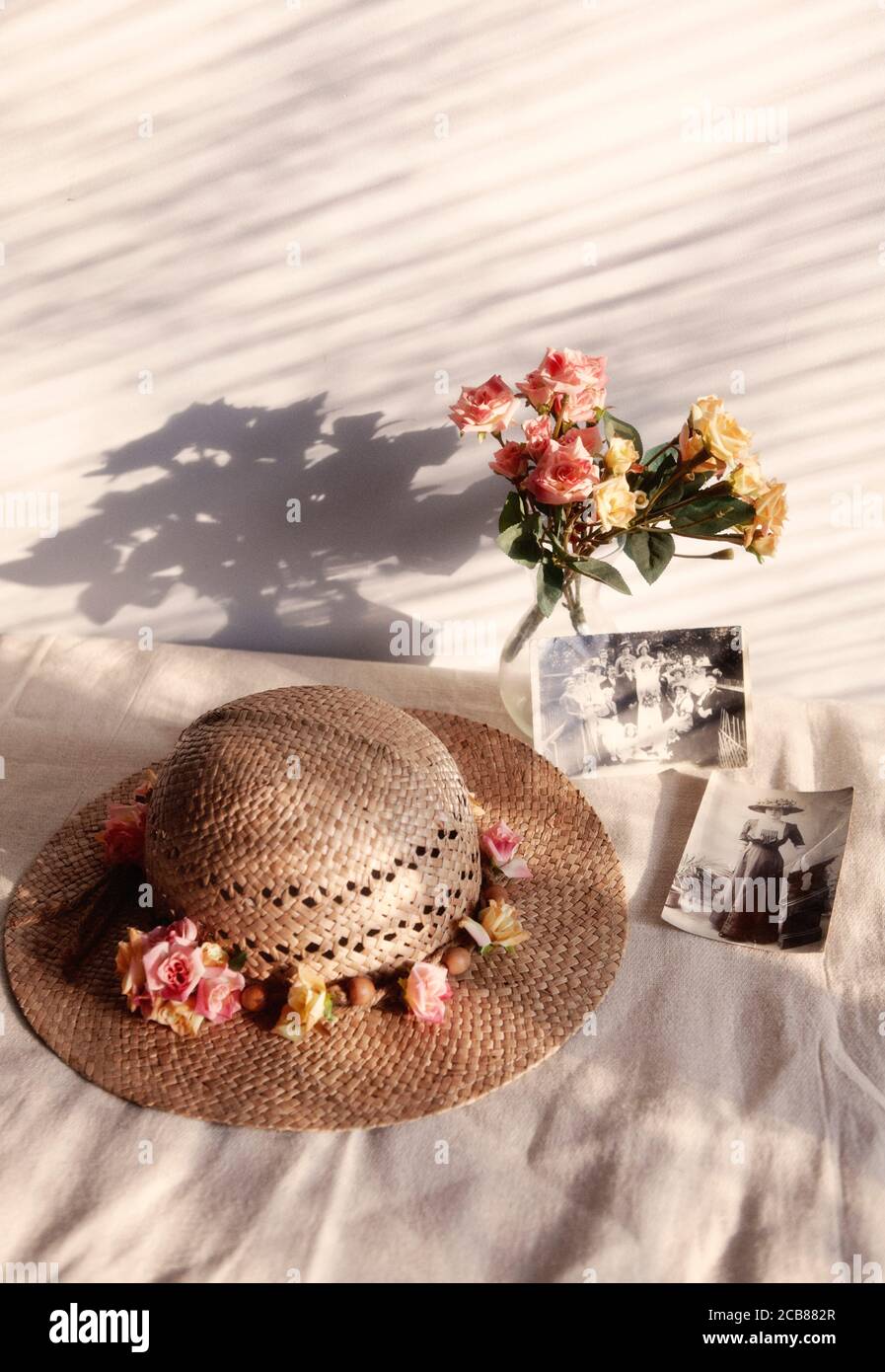 https://c8.alamy.com/comp/2CB882R/straw-hat-with-vase-of-roses-and-old-photographs-2CB882R.jpg