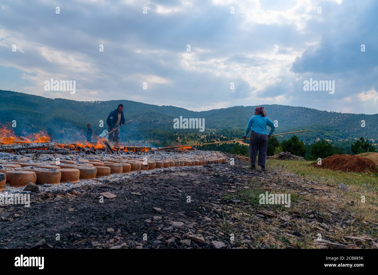 Mihaliccik, Eskisehir/Turkey-July 26 2020: Woman workers dry clay pottery via burning wooden on ground in open air. Stock Photo