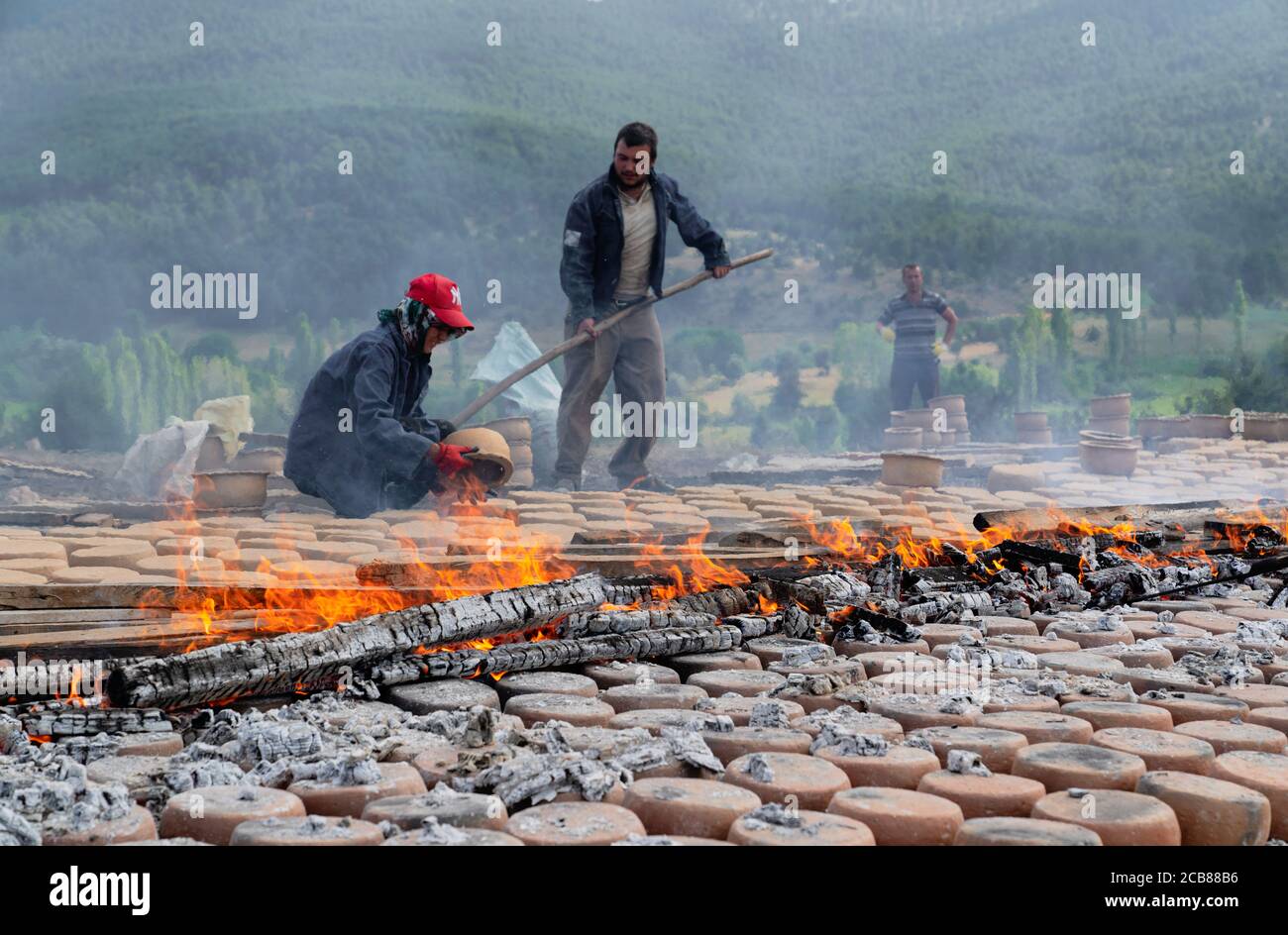 Mihaliccik, Eskisehir/Turkey-July 26 2020: Woman workers dry clay pottery via burning wooden on ground in open air. Stock Photo