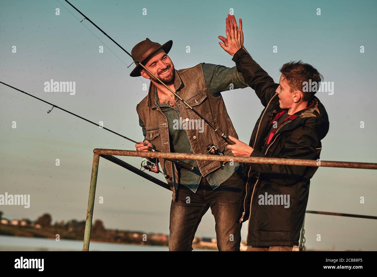 Father and son stand on pier. They fish and give each other five Stock Photo