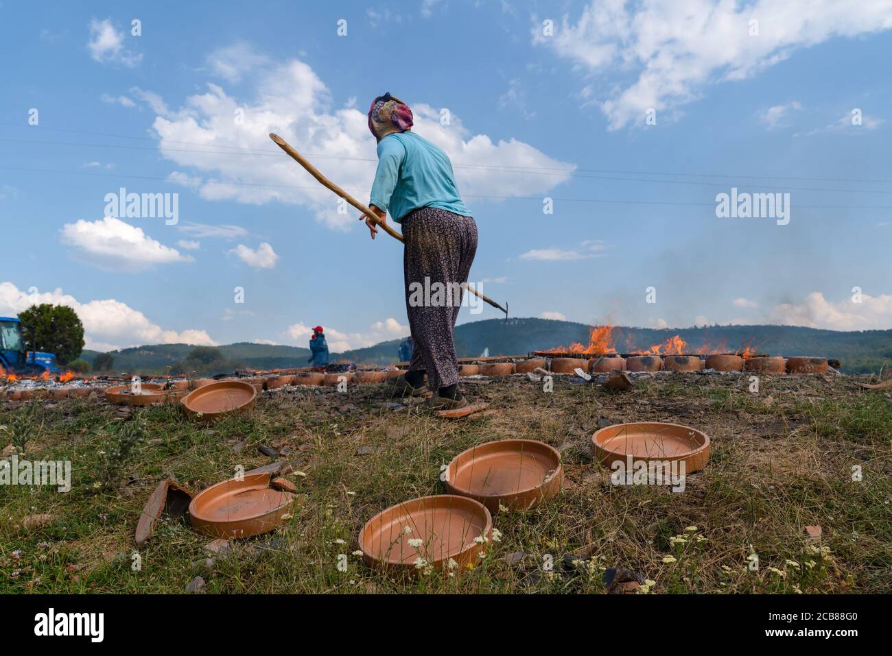 Back view of woman worker dries clay pottery via burning wooden on ground in open air. Mihaliccik, Eskisehir/Turkey Stock Photo