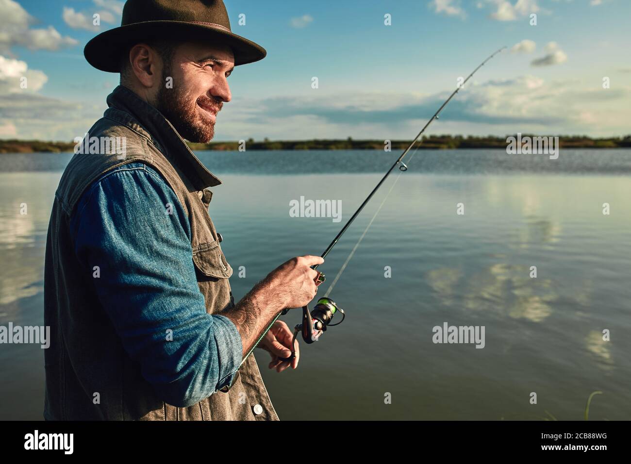 Caucasian adult bearded men stand near lake and hold fishing rod