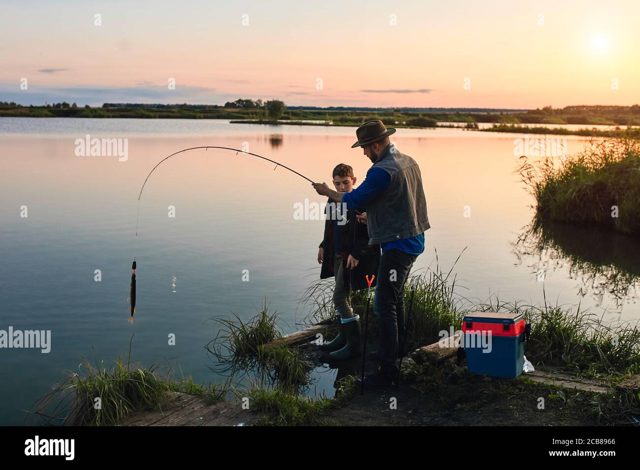 Father and son caught first big fish together. They get it out of lake. They happy. Stock Photo