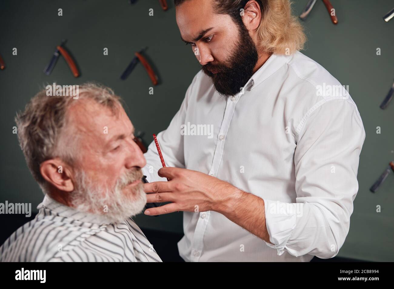 young bearded barber concentrated on working process, close up portrait