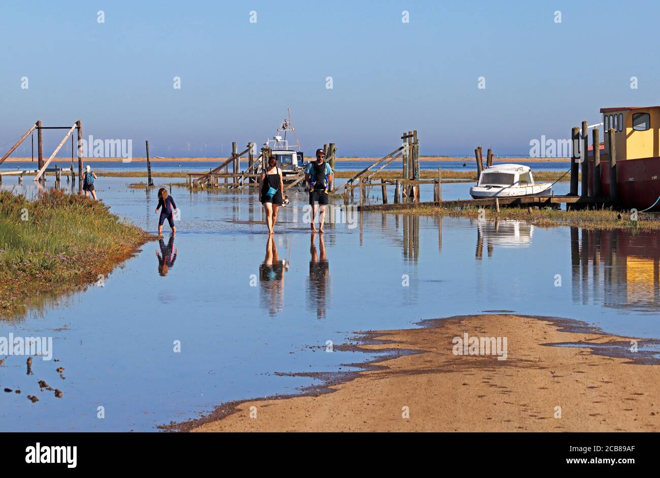 A family paddling through overtopped flood water by the Harbour Channel in North Norfolk at Thornham, Norfolk, England, United Kingdom. Stock Photo