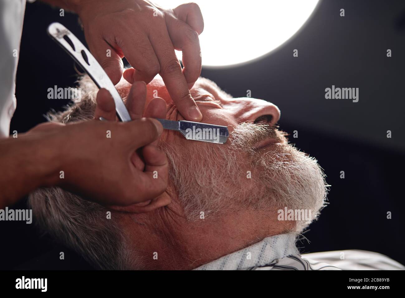 stylist using a traditional tool to shave facial hair on face, close up