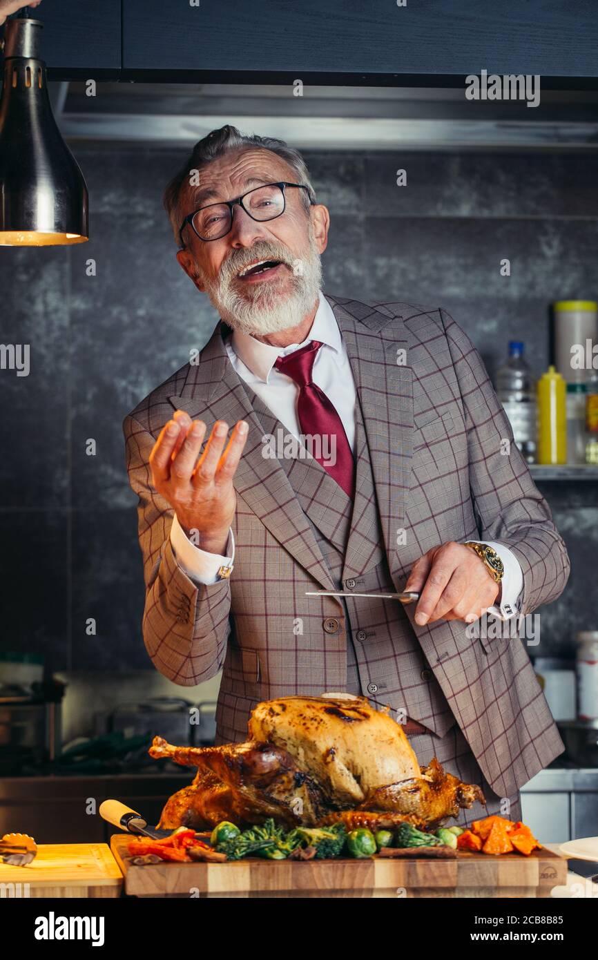 https://c8.alamy.com/comp/2CB8B85/old-man-dressed-in-rich-tailored-suit-carving-delicious-succulent-charcoal-roast-chicken-with-knife-on-a-wooden-cutting-board-family-holidays-and-cel-2CB8B85.jpg