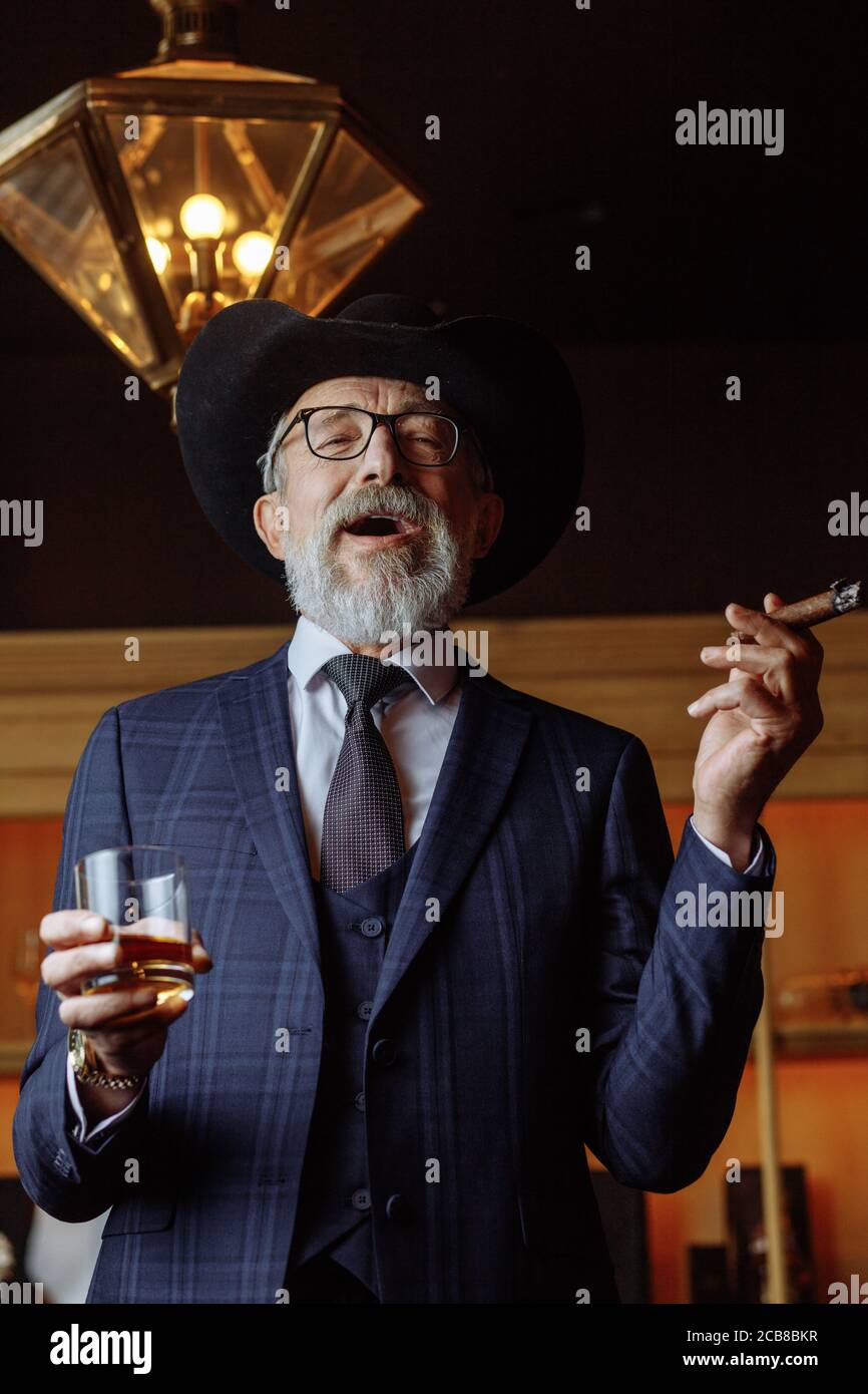 Thoughtful, selective, male aged investor in glasses, smoking cigar ...