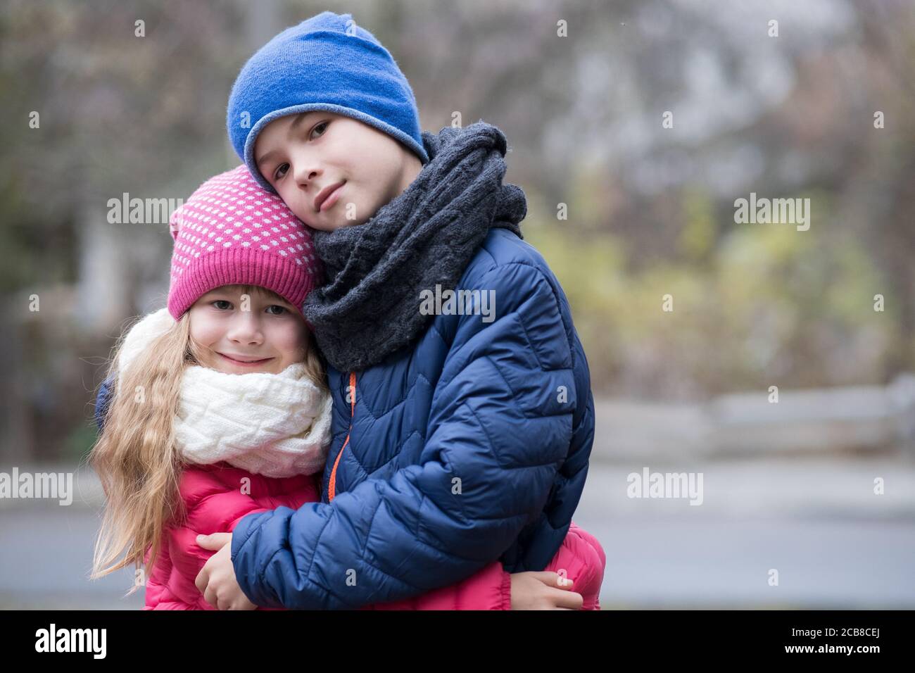 Two children boy and girl hugging each other outdoors wearing warm clothes in cold autumn or winter weather. Stock Photo