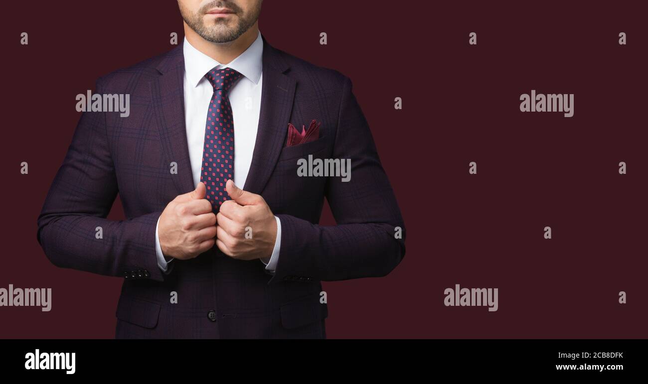 Sharp dressed man in jacket and tie isolated on dark red background. Picture for advertising a men's clothing store. A symbol of success and masculini Stock Photo