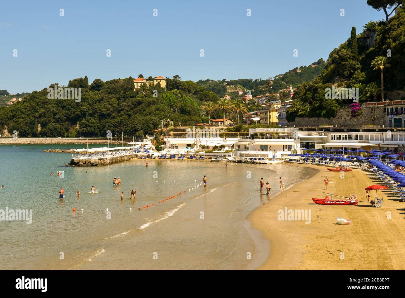 Elevated view of a sandy beach with vacationers in the waves of the shore and a wooded hill in the background in summer, Lerici, La Spezia, Italy Stock Photo