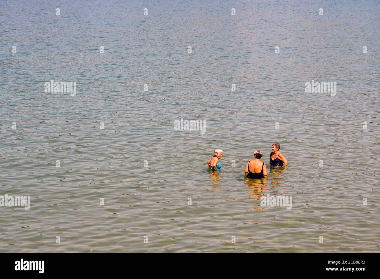 Elevated view of three elderly ladies refreshing and chatting in the water on the seashore in summer, Liguria, Italy Stock Photo