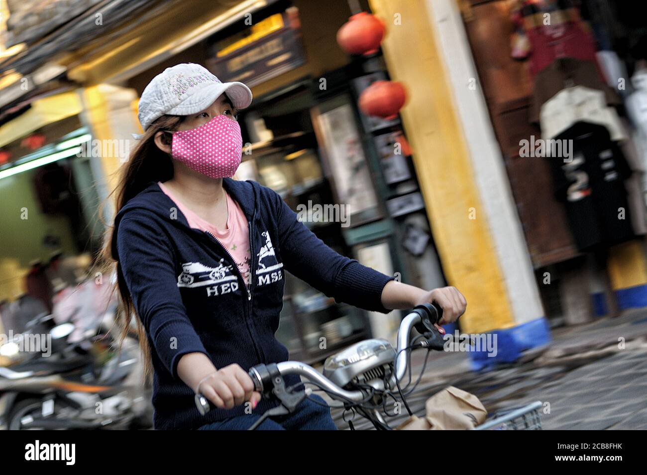 Woman on bicycle wearing a facial mask in Hoi An, Vietnam Stock Photo