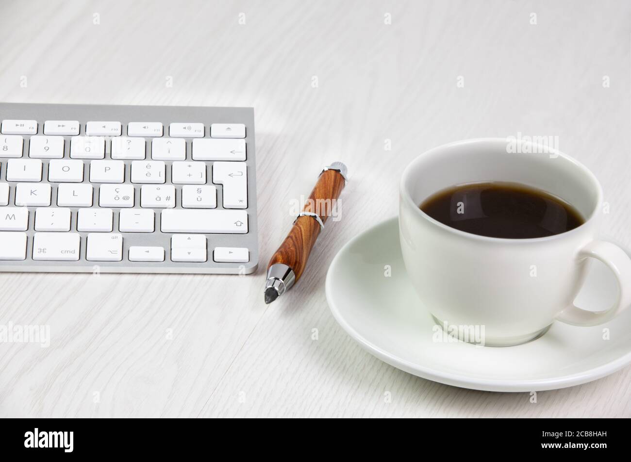 Office work station with roasted coffee beans cup, pencil and keyboard on white wooden table Stock Photo