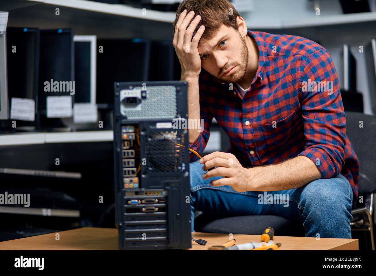 IT technician dressed in stylish shirt and jeans holding his forehead and repairing broken pc computer. close up photo. Stock Photo