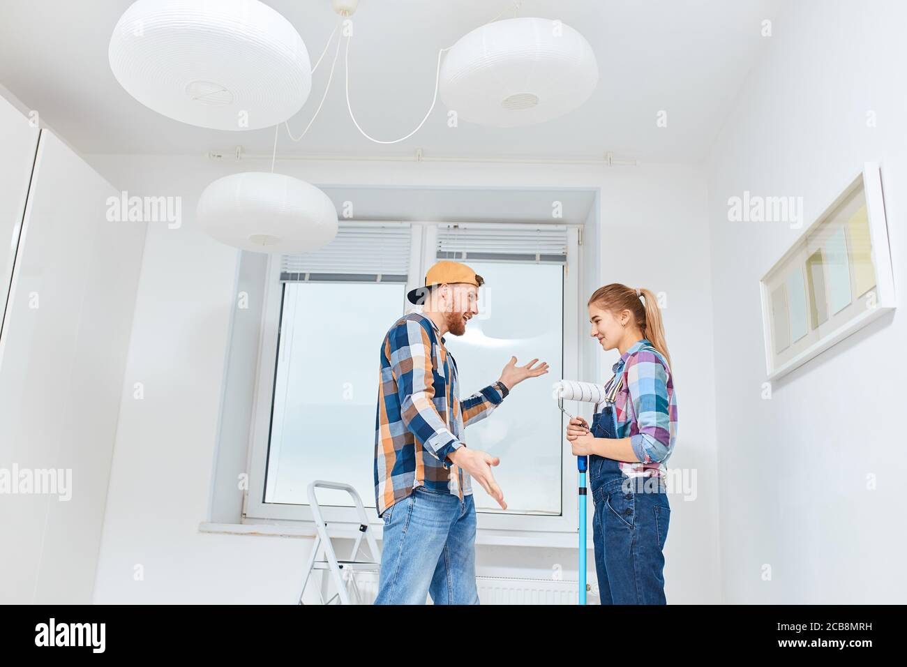 People, renovation concept - Young woman and man discussing colour of paint for walls standing in empty white room Stock Photo