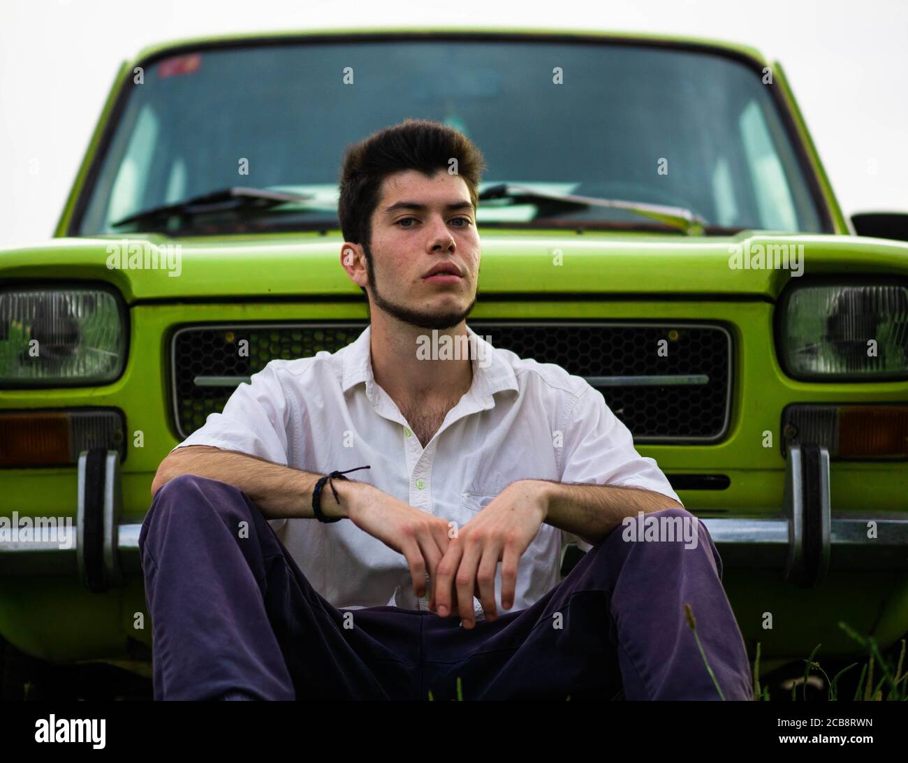 Young Caucasian man sitting near a vintage green car Stock Photo