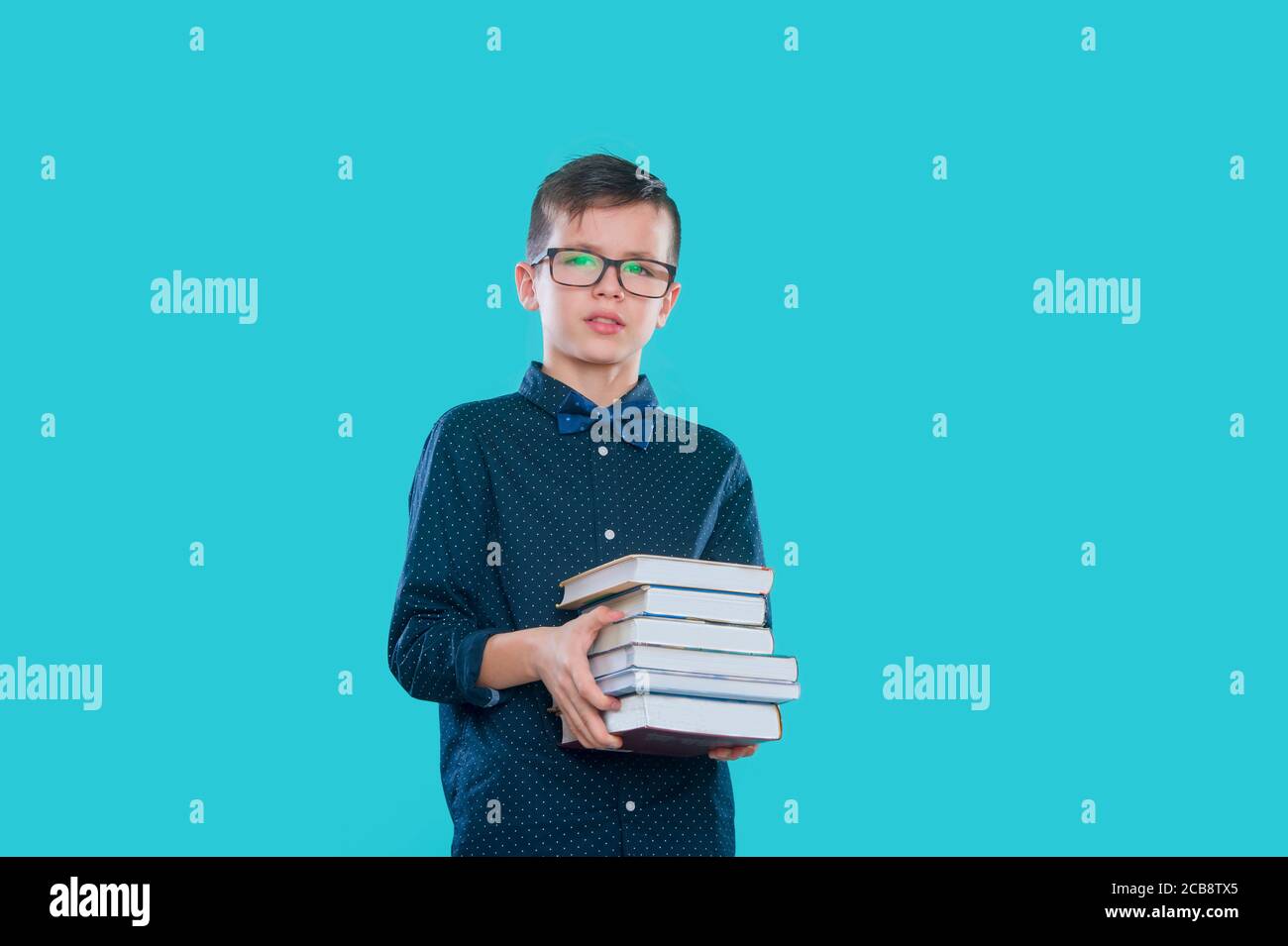 Little cheerful school boy wearing glasses holding a book over blue ...