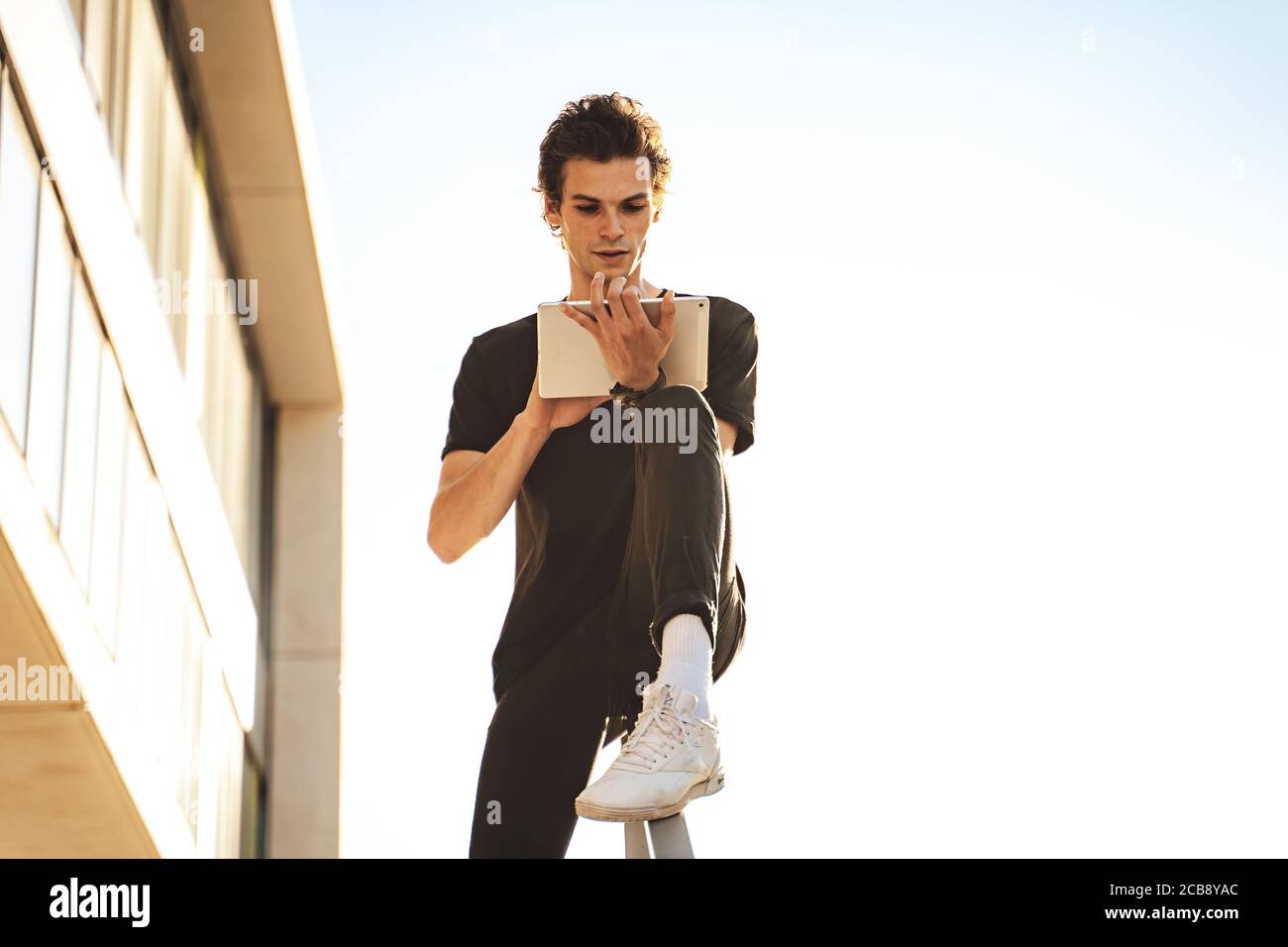 Handsome young man using digital tablet while sitting on railing against clear sky Stock Photo